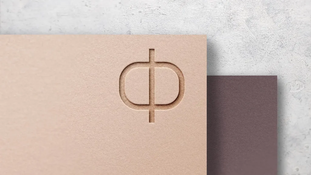 Gros plan d'un symbole stylisé gravé en creux sur un papier texturé beige clair, avec un papier texturé plus foncé en arrière-plan, sur un fond texturé gris clair.