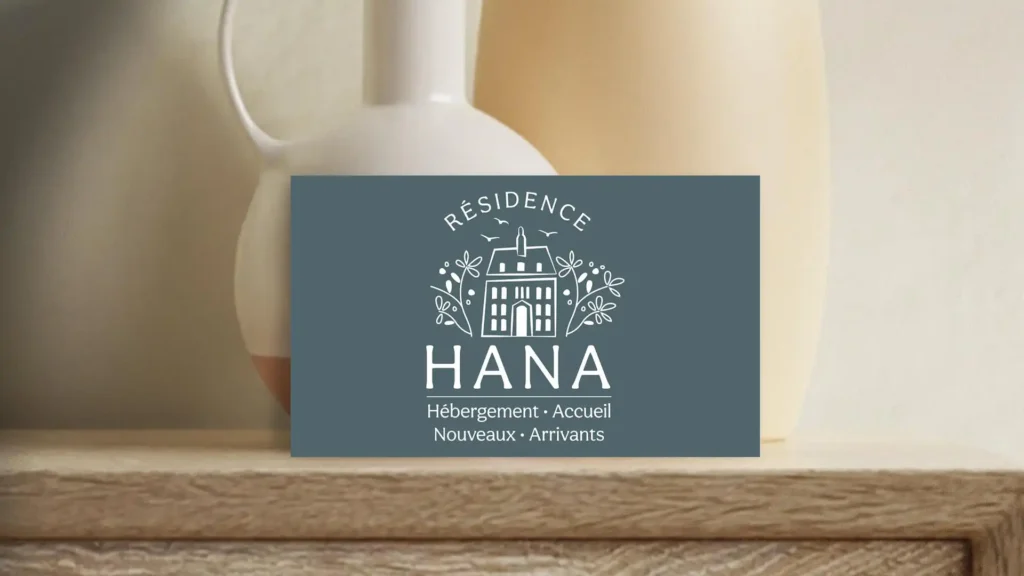 Carte de visite bleue avec le logo 'Résidence Hana', un dessin de maison et les mots 'Hébergement - Accueil - Nouveaux Arrivants', sur un fond de céramiques claires.