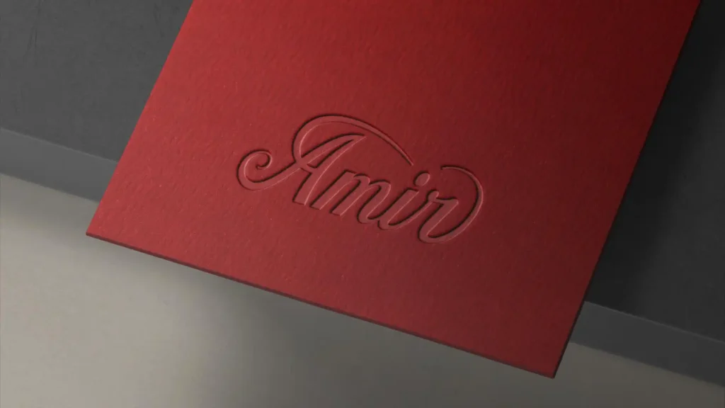 Gros plan d'une carte ou d'un papier rouge texturé, avec le mot "Amir" écrit en lettres cursives en relief dans la même couleur.