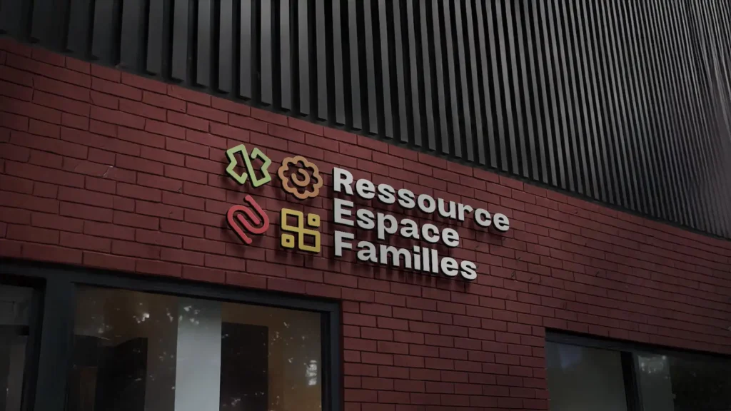 Logo coloré et inscription "Ressource Espace Familles" en relief sur un mur de briques rouges, avec une façade de bâtiment moderne en arrière-plan.