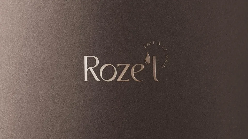 Logo 'Roze'l' en relief clair sur un fond texturé brun foncé, avec la mention 'Fait à la main' en petit texte circulaire.