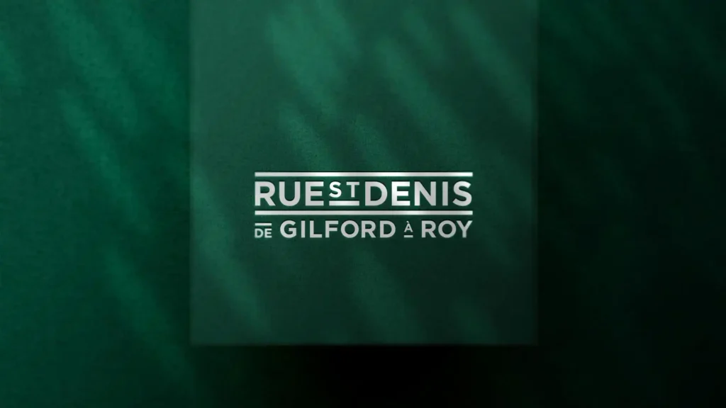 Gros plan d'une carte ou d'un document vert foncé texturé avec l'inscription "RUE ST DENIS" en lettres argentées et "DE GILFORD À ROY" en plus petit en dessous.