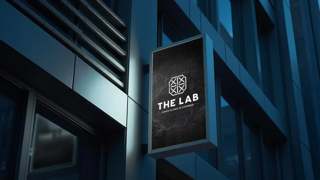Enseigne rectangulaire noire avec le logo "THE LAB" accrochée à un bâtiment moderne.