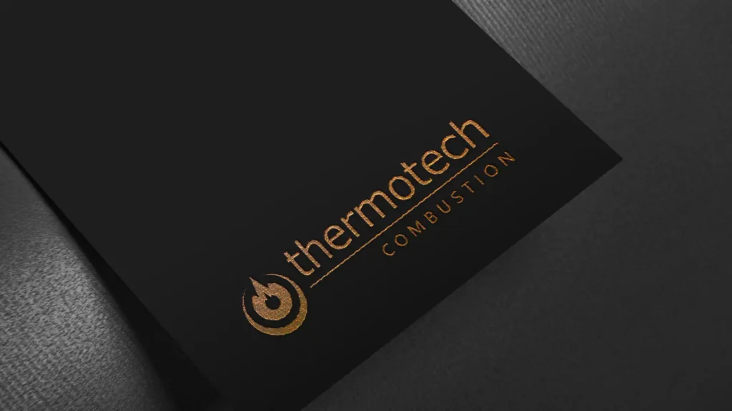 Gros plan d'une carte noire avec le logo "thermotech COMBUSTION" en dorure brillante, incluant une flamme stylisée.