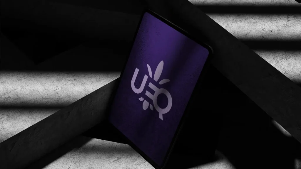 Maquette d'une tablette à l'écran violet affichant un logo blanc "UEQ", placée en diagonale sur des marches d'escalier en béton avec des ombres marquées.