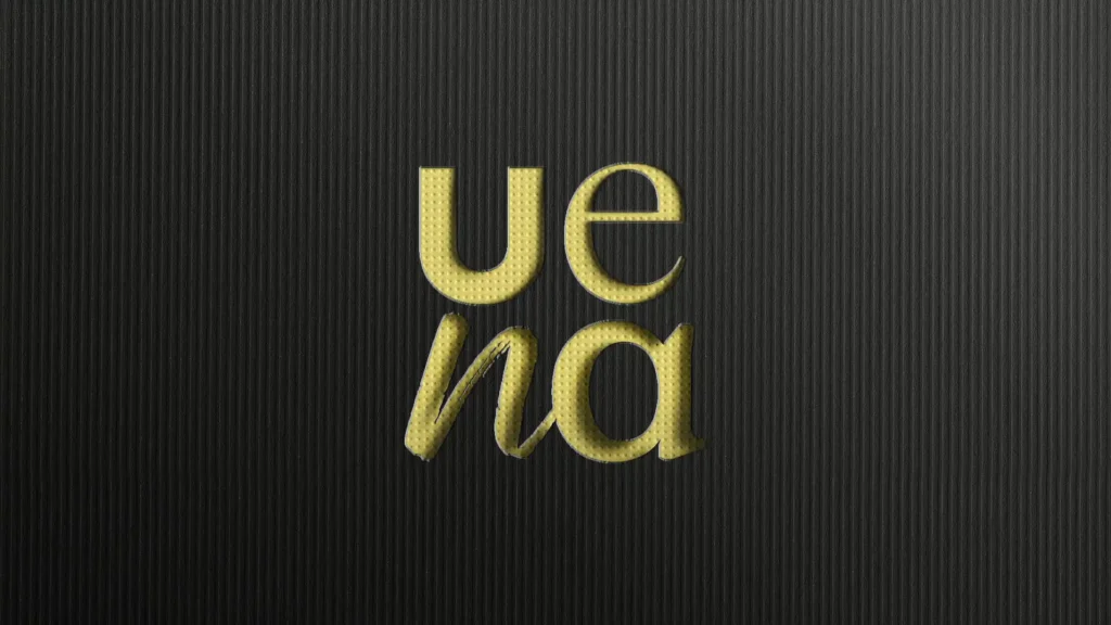 Gros plan d'un fond noir texturé avec le mot "Uena" écrit en lettres dorées et légèrement en relief, avec "Ue" au-dessus de "na".