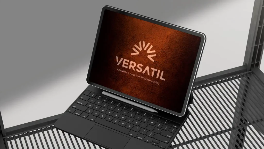 Maquette d'une tablette noire avec un clavier et un stylet, présentant le logo "VERSATIL" et la mention "Analytics & AI-Driven Decision Making" sur un écran à fond orangé texturé.