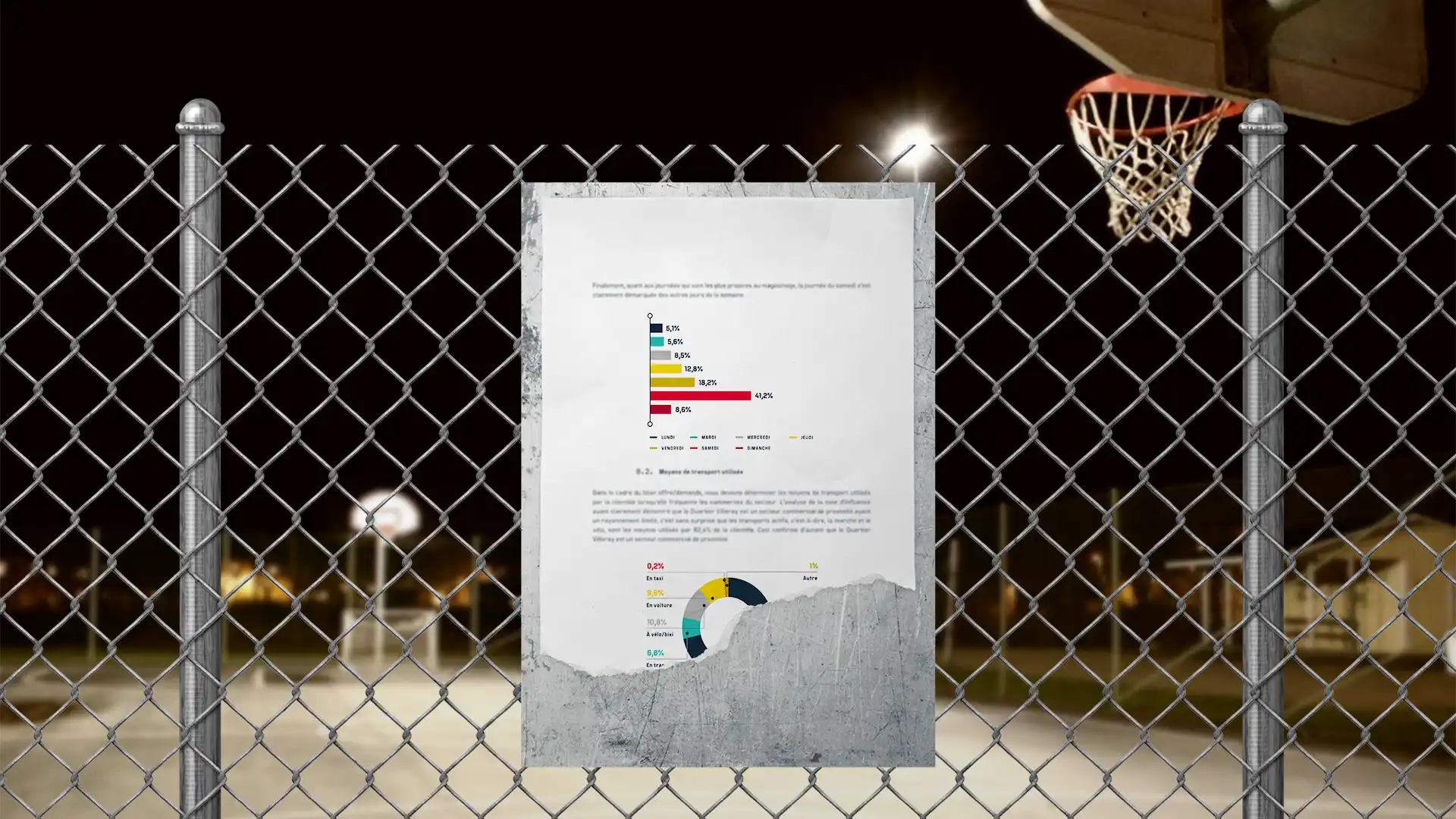 Un document avec des graphiques est fixé sur une clôture en grillage devant un terrain de basketball éclairé la nuit.